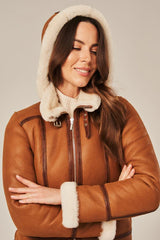 Woman wearing a brown leather jacket with white fur trim on a neutral background